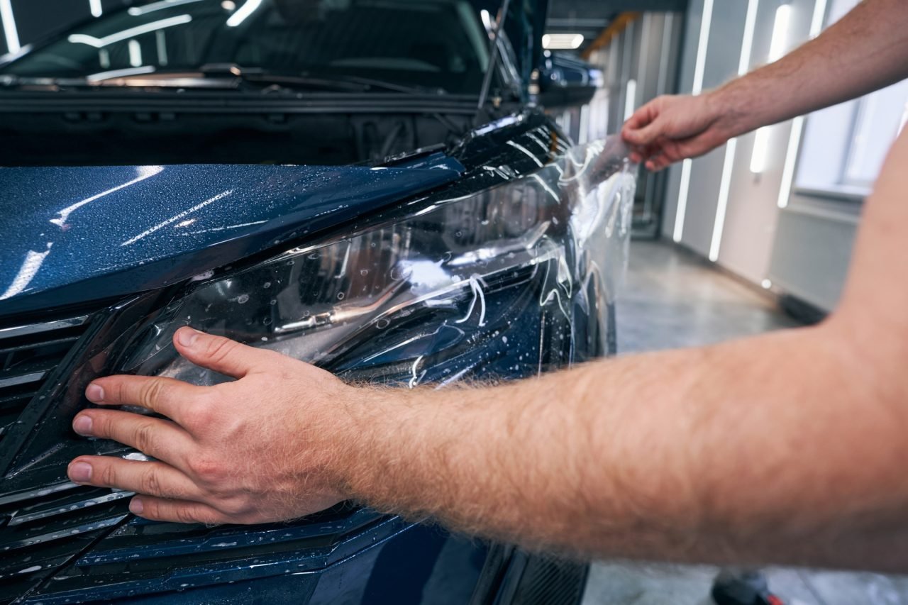 closeup-car-service-technician-man-putting-protective-film-on-headlamp.jpg